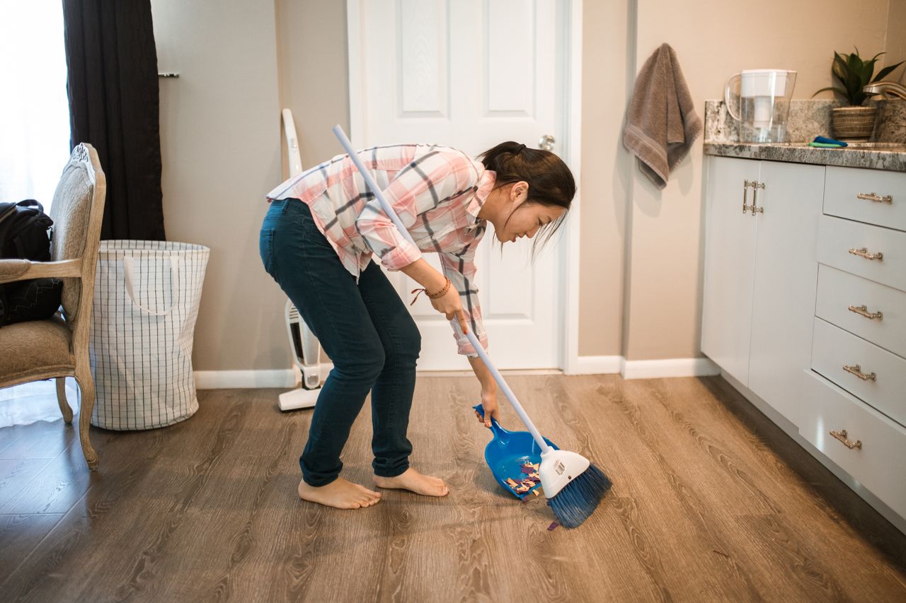 An Asian woman performing cleaning chores by sweeping the floor indoors.